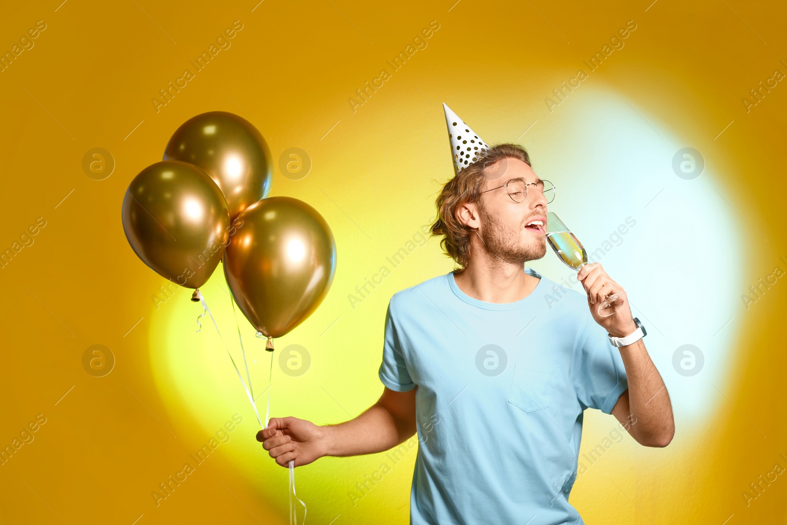 Photo of Portrait of happy man with champagne in glass and party balloons on color background