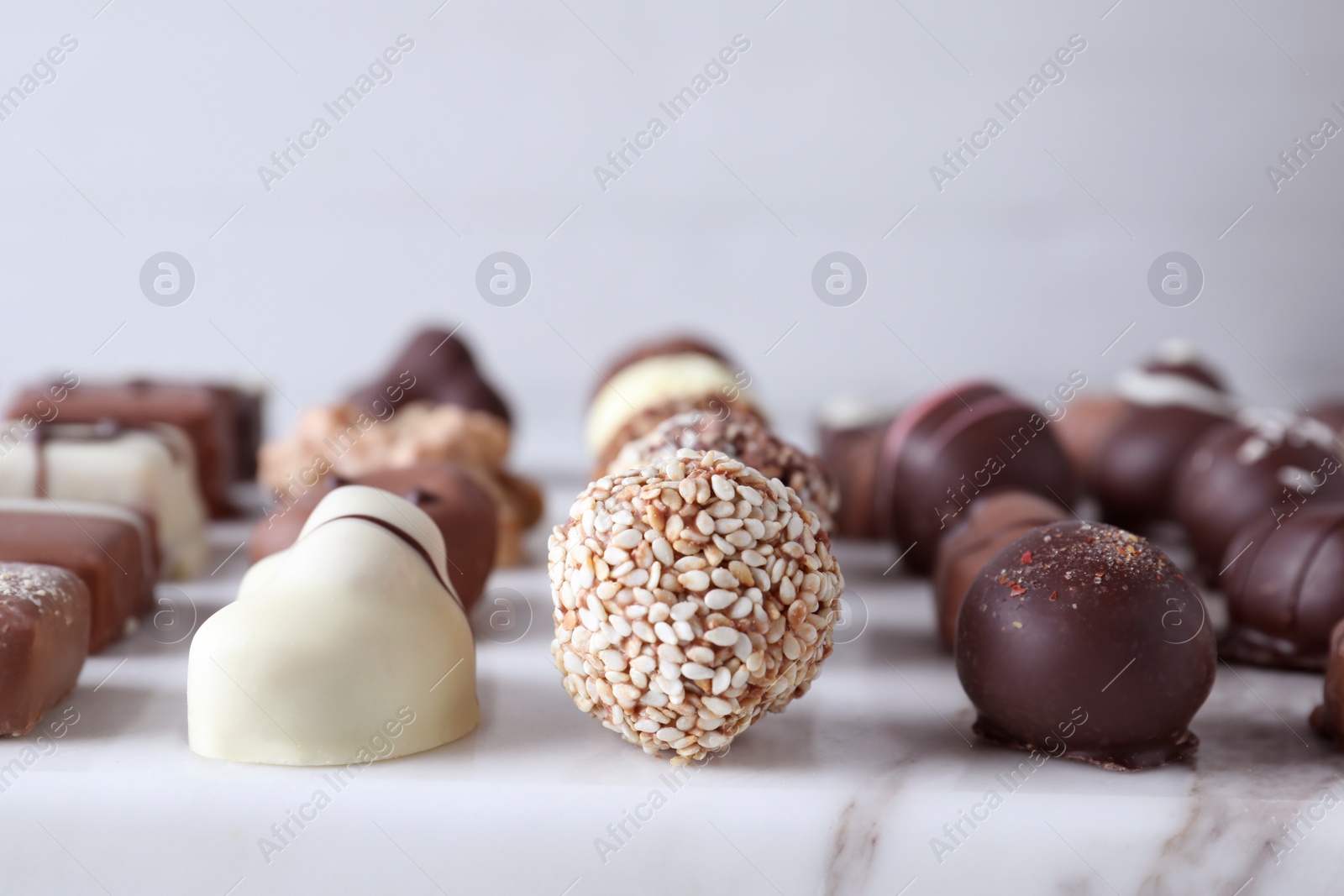 Photo of Different tasty chocolate candies on white marble table