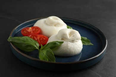 Photo of Delicious burrata cheese with basil and cut tomato on black table