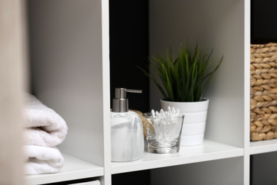 Photo of Dispenser, cotton swabs and plant on white shelf in bathroom