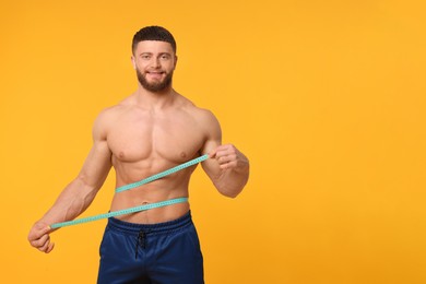 Photo of Happy athletic man measuring waist with tape on orange background, space for text. Weight loss concept