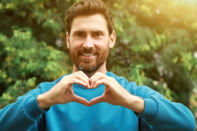 Photo of Happy man making heart gesture outdoors, focus on hands