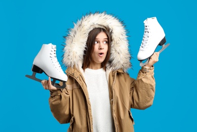 Emotional woman with ice skates on light blue background