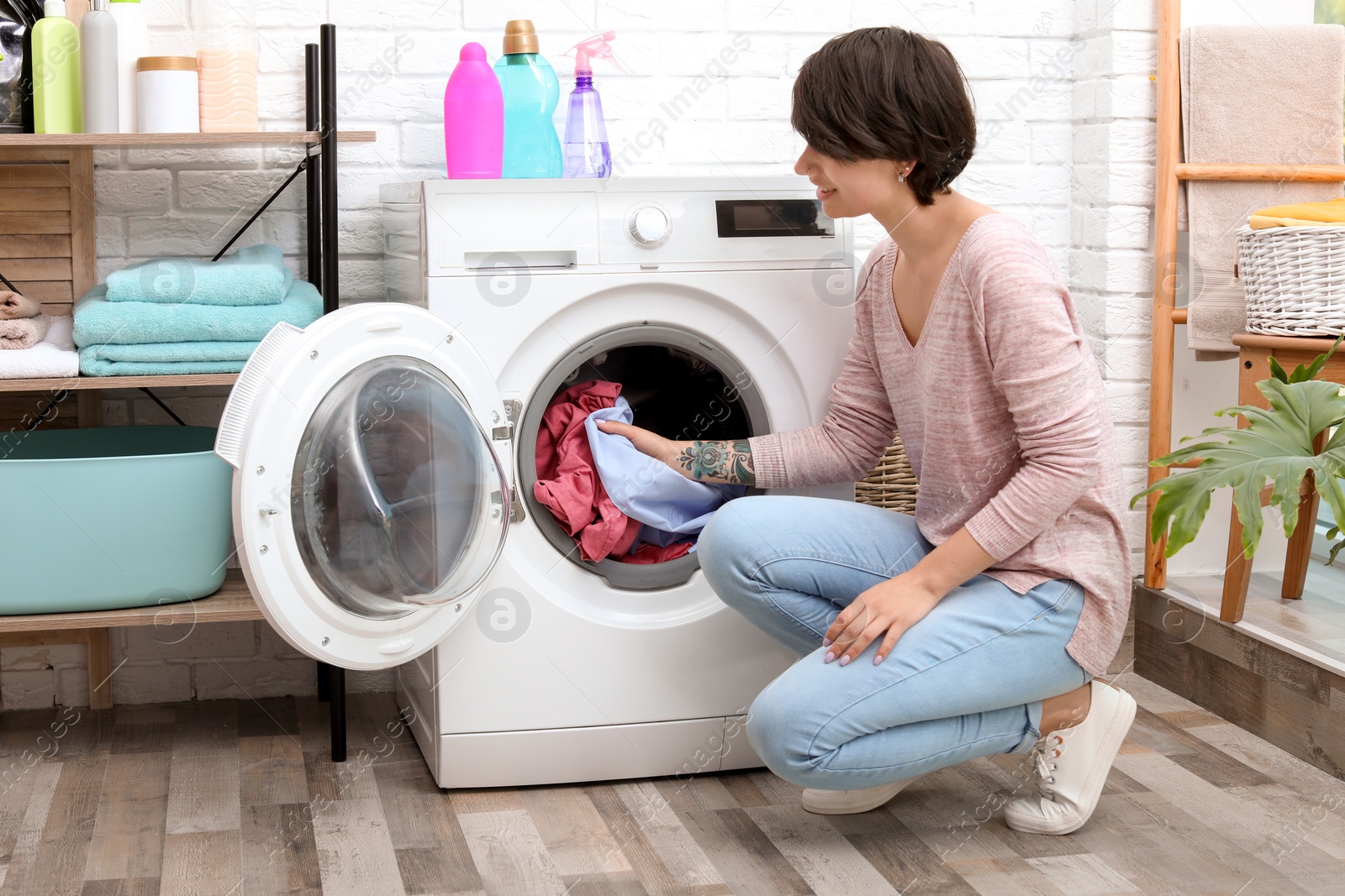 Photo of Young woman putting clothes into washing machine at home