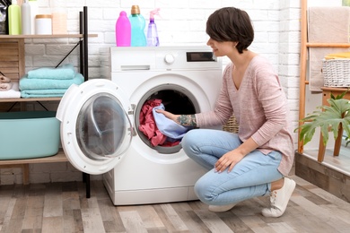 Photo of Young woman putting clothes into washing machine at home