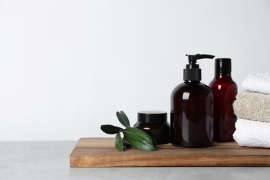 Photo of Different cosmetic products, towels and leaves on grey table. Space for text