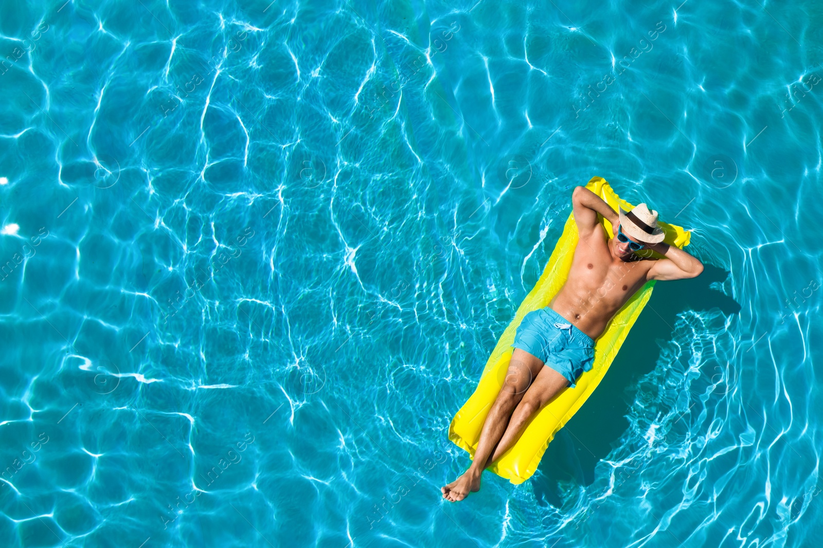 Image of Young man with inflatable mattress in swimming pool, top view. Space for text