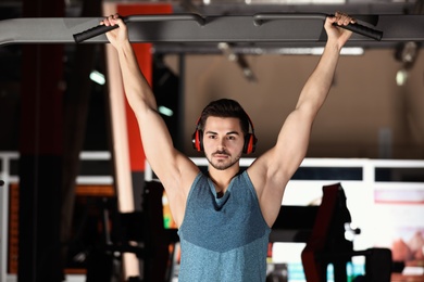 Photo of Young man with headphones listening to music and working out at gym