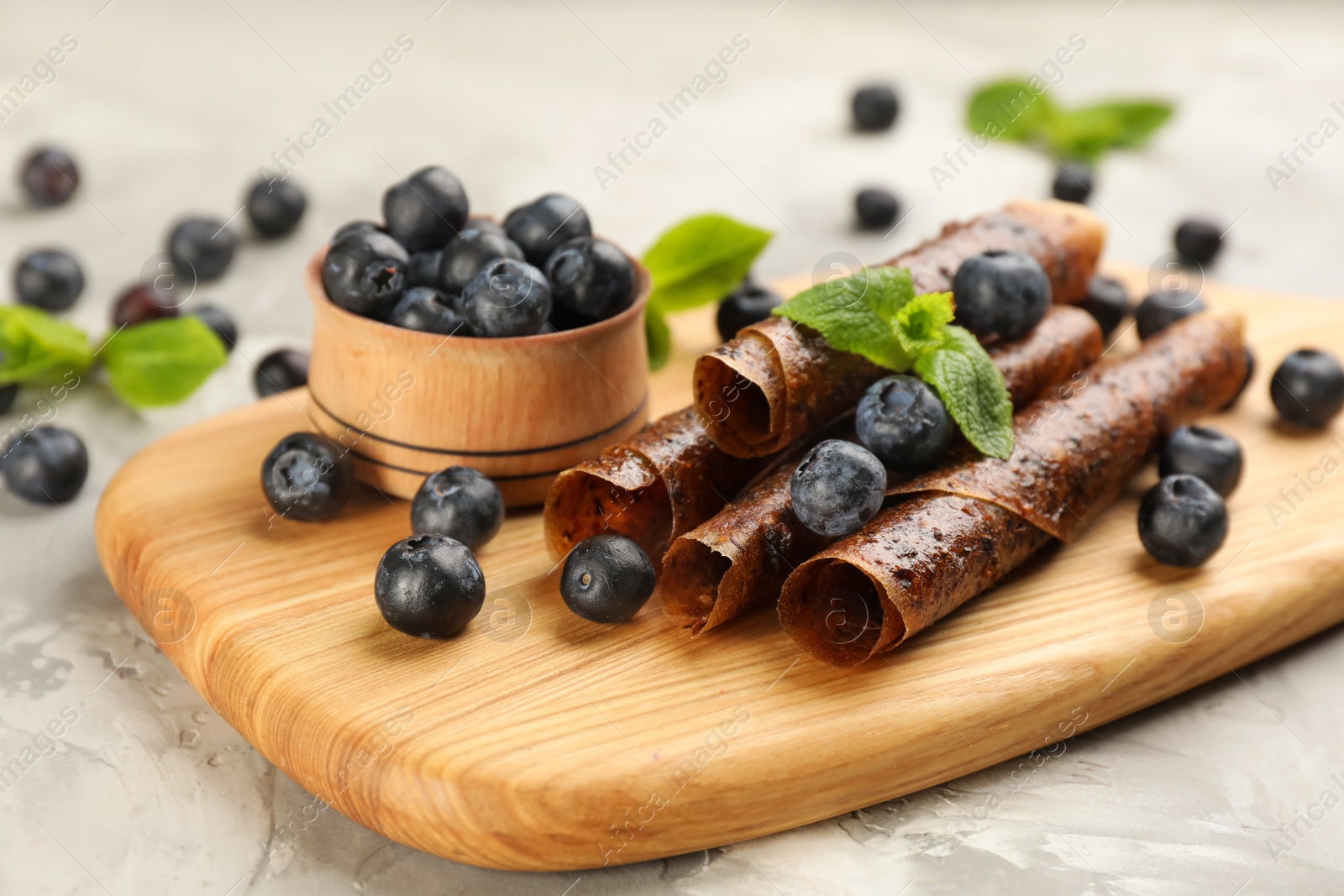 Photo of Delicious fruit leather rolls and blueberries on grey table, closeup