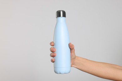 Photo of Woman holding thermo bottle of drink on light background, closeup