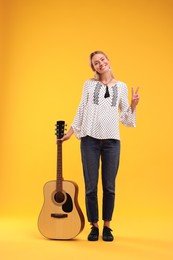 Photo of Happy hippie woman with guitar showing peace gesture on yellow background