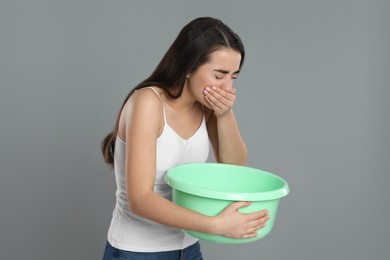 Photo of Young woman with basin suffering from nausea on grey background. Food poisoning