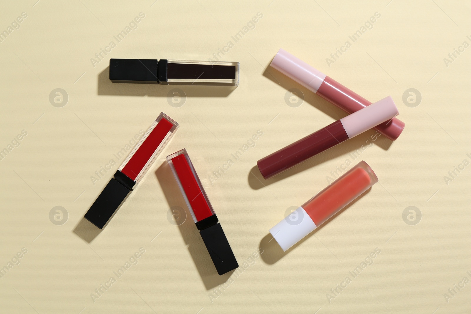 Photo of Different lip glosses on pale yellow background, flat lay