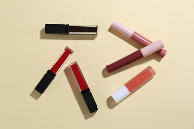 Different lip glosses on pale yellow background, flat lay