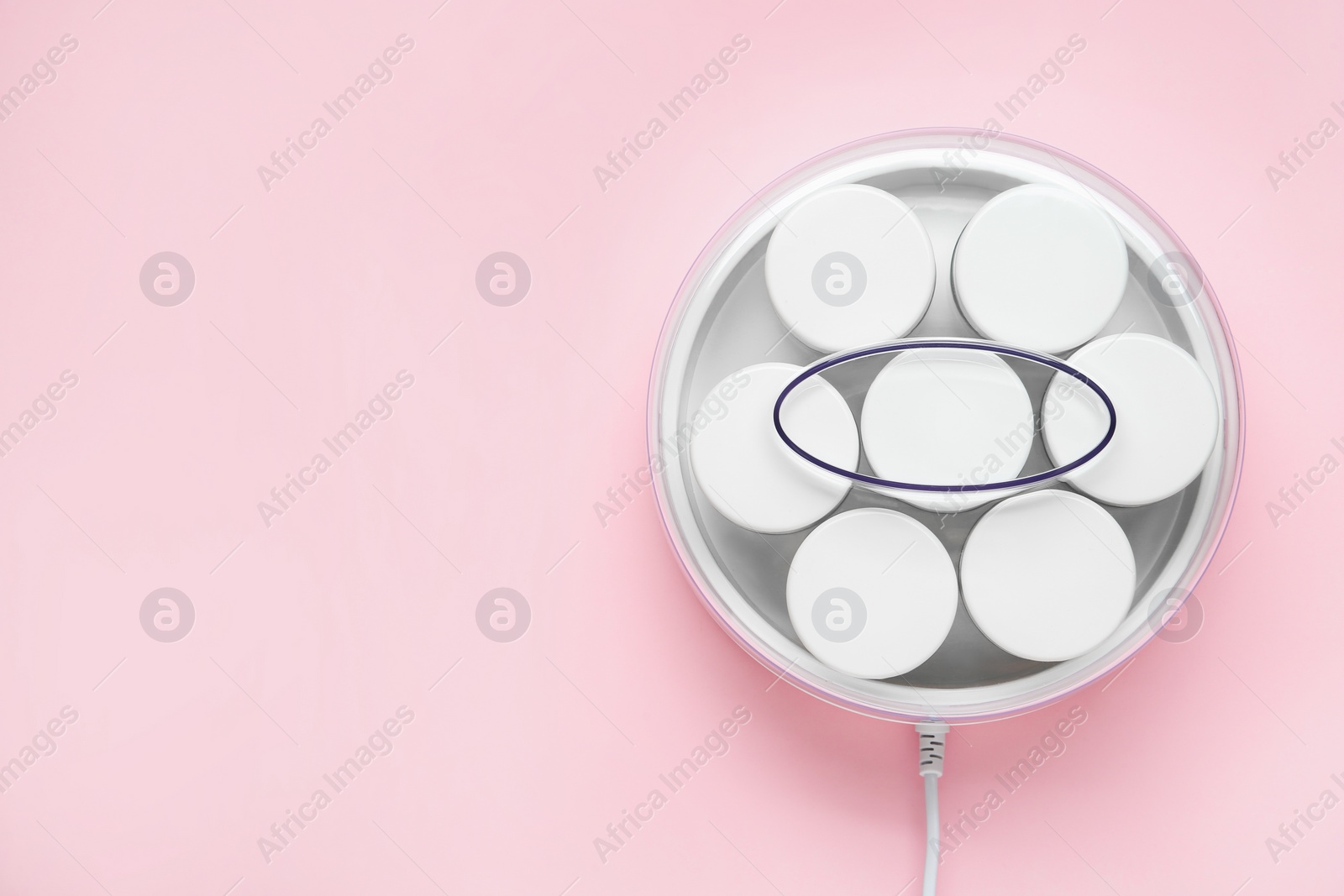 Photo of Modern yogurt maker with jars on pink background, top view. Space for text