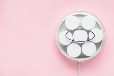 Modern yogurt maker with jars on pink background, top view. Space for text