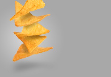 Tasty tortilla chips falling on grey background, space for text