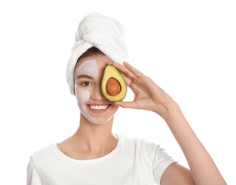 Happy young woman with organic mask on her face holding avocado against white background