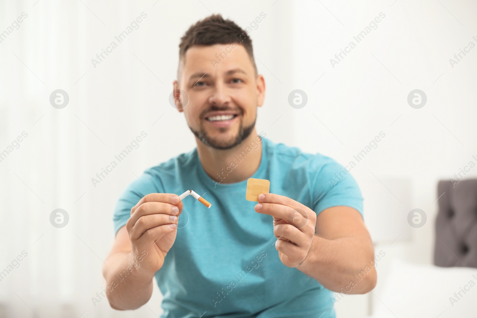 Photo of Happy man with nicotine patch and cigarette in bedroom, focus on hands
