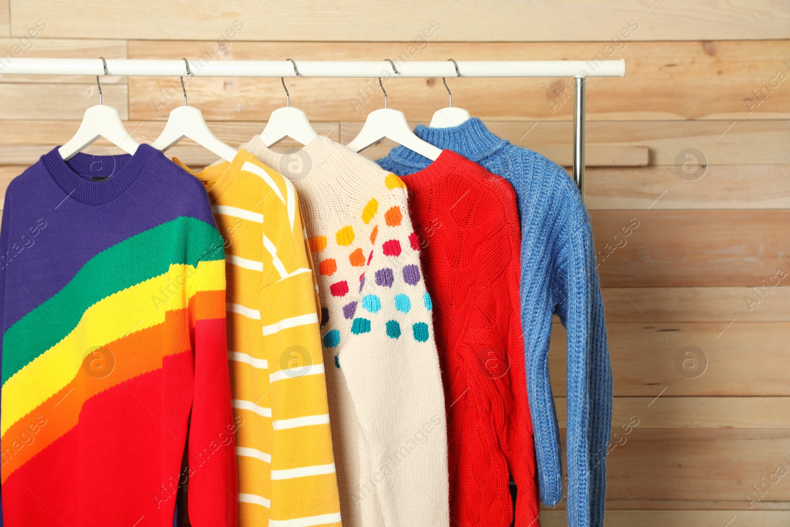 Photo of Collection of warm sweaters hanging on rack against wooden background