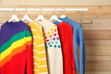 Collection of warm sweaters hanging on rack against wooden background