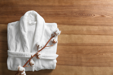 Photo of Clean folded bathrobe and branch of cotton on wooden background, top view. Space for text