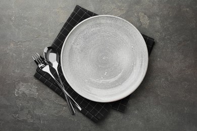 Empty plate, cutlery and checkered napkin on grey textured table, top view