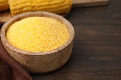 Raw cornmeal in bowl on wooden table, closeup. Space for text