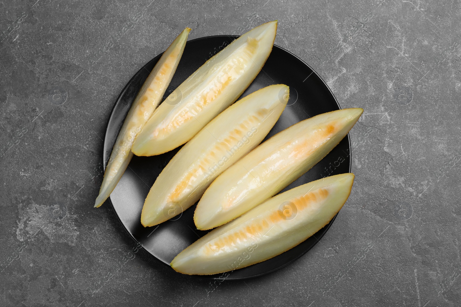 Photo of Slices of delicious honey melon on black table, top view