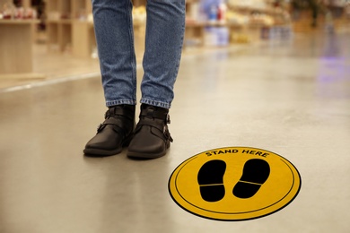 Image of Keep social distance as preventive measure during coronavirus outbreak. Yellow warning sign on floor near woman, closeup