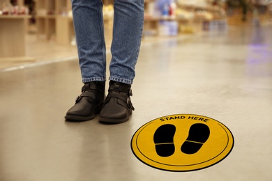 Keep social distance as preventive measure during coronavirus outbreak. Yellow warning sign on floor near woman, closeup