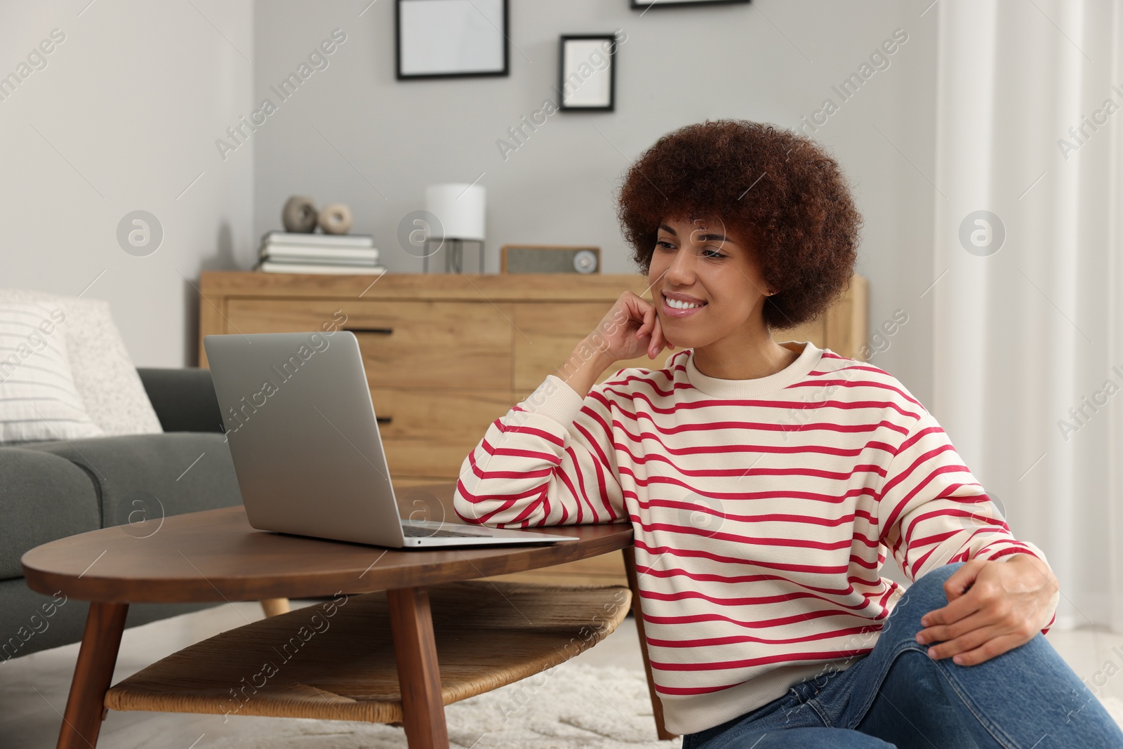 Photo of Beautiful young woman using laptop at wooden coffee table in room