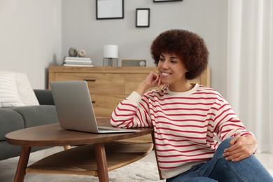 Beautiful young woman using laptop at wooden coffee table in room