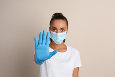 Photo of Woman in protective mask showing stop gesture on beige background. Prevent spreading of COVID‑19