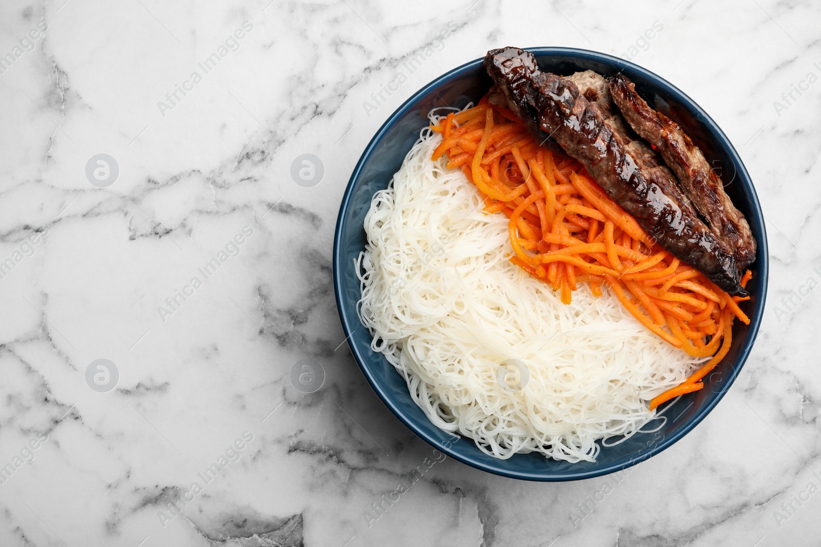 Photo of Tasty cooked rice noodles with meat and carrot on white marble table, top view