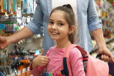 Photo of Little girl with father choosing school stationery in supermarket