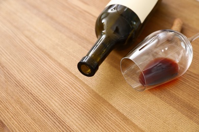 Overturned glass and bottle of wine on wooden background. Space for text