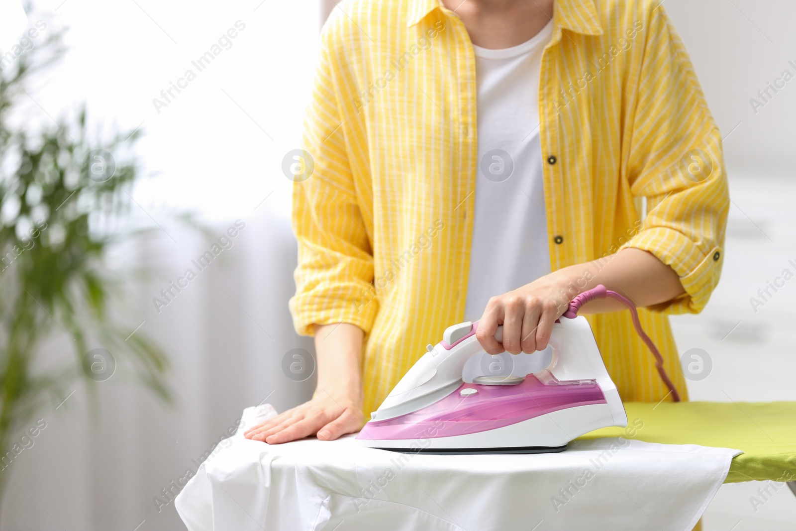 Photo of Young woman ironing clean laundry on board indoors, closeup