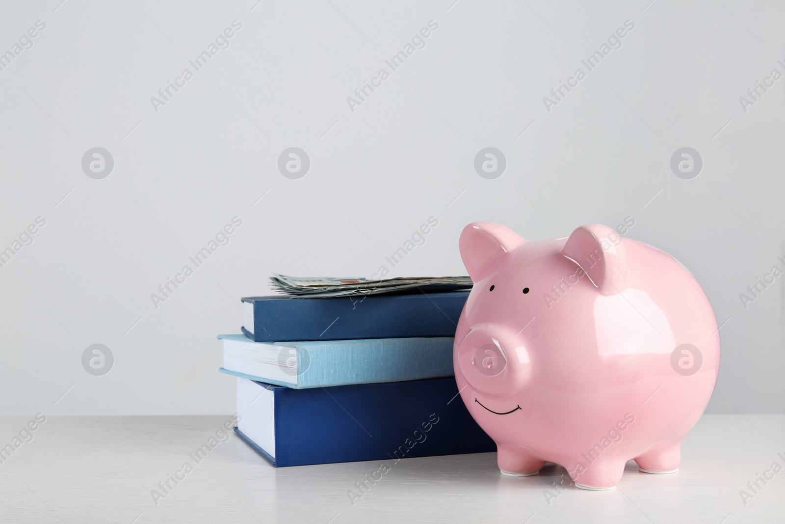 Photo of Piggy bank with dollars and books on table against white background. Space for text