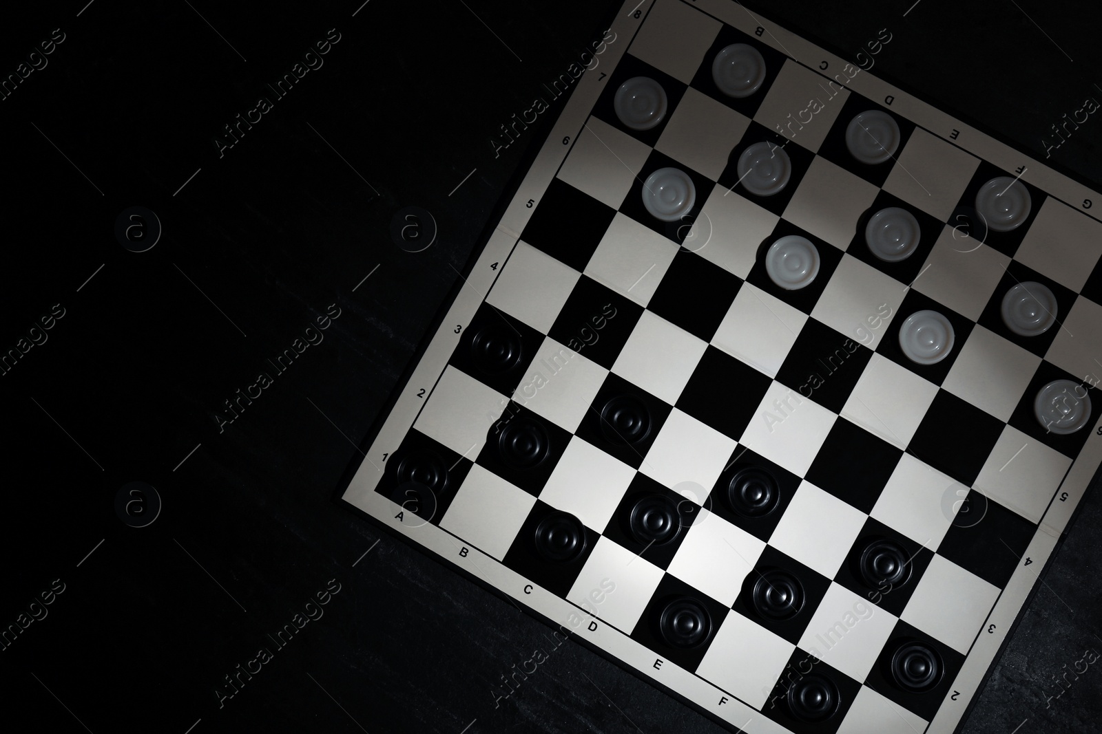 Photo of Checkerboard with game pieces on black table, top view. Space for text