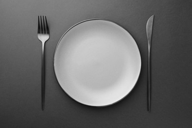 Photo of Empty plate, fork and knife on grey table, top view
