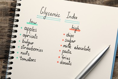 Notebook with products of low and high glycemic index and pen on wooden table, top view