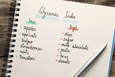 Photo of Notebook with products of low and high glycemic index and pen on wooden table, top view