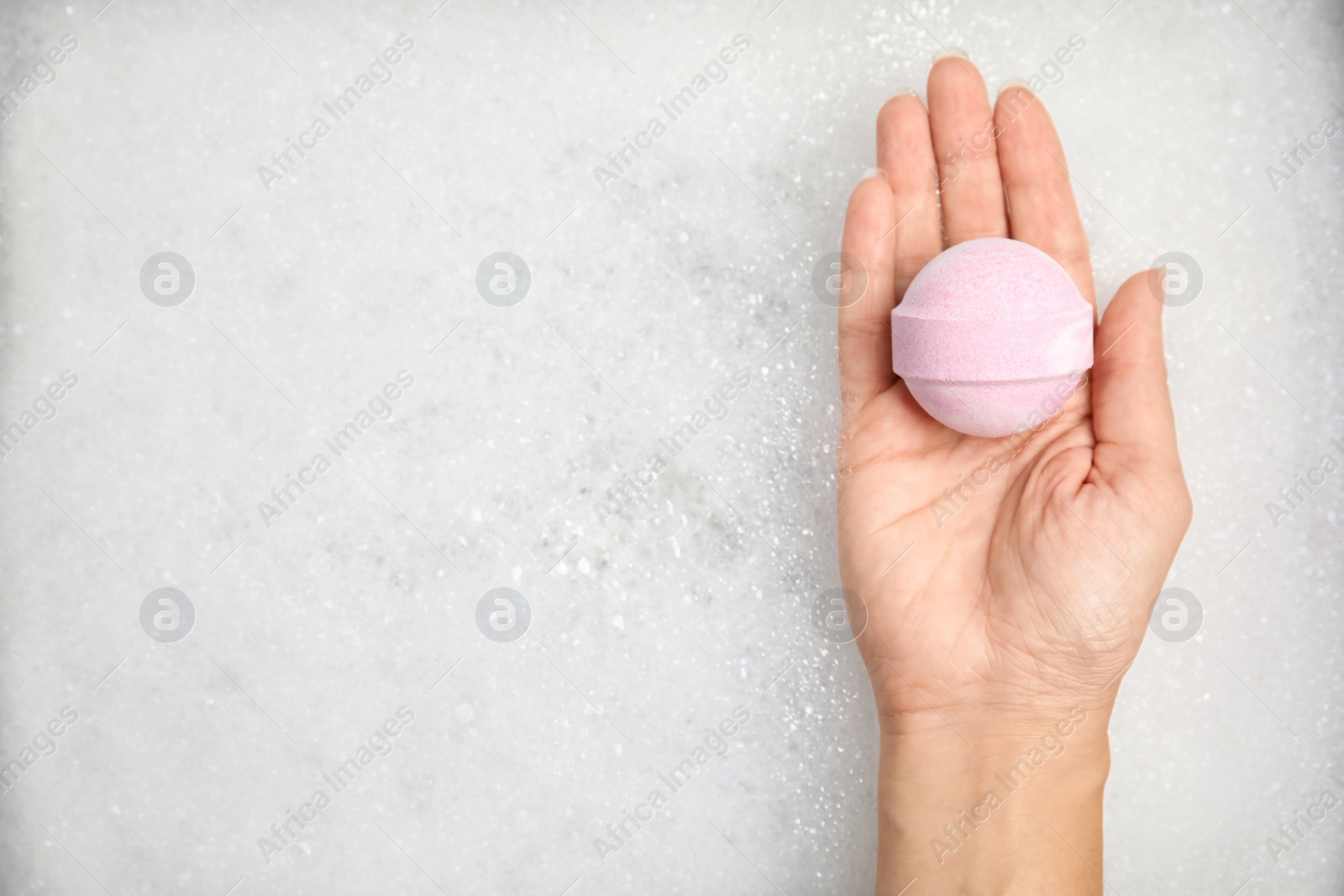 Photo of Woman holding bath bomb over foam, top view. Space for text