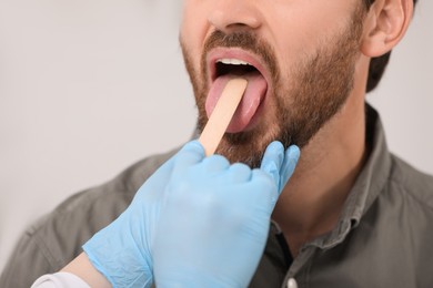 Doctor examining man`s oral cavity with tongue depressor on blurred background, closeup