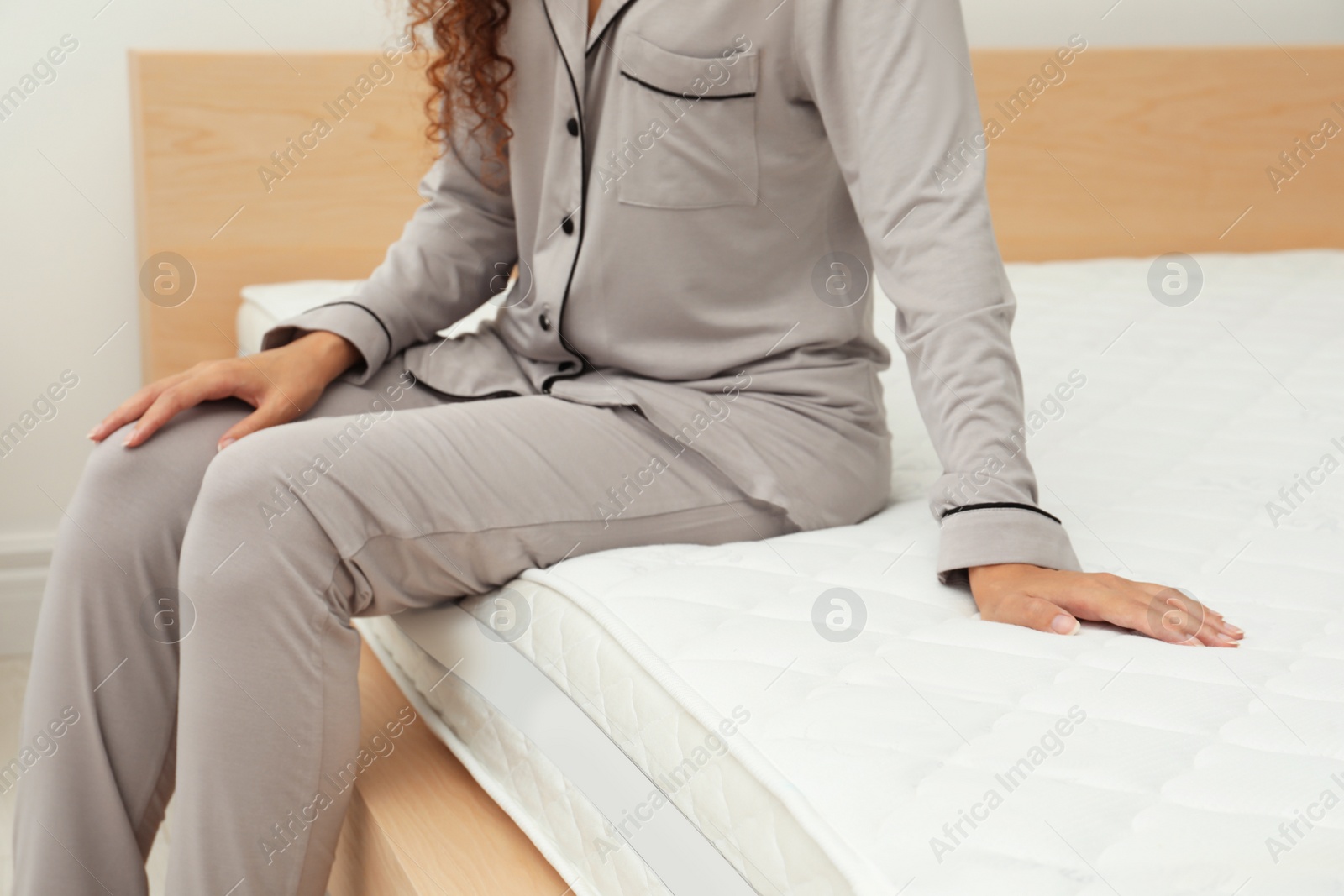 Photo of African American woman sitting on soft mattress in bedroom, closeup