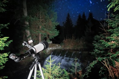 Photo of Modern telescope near waterfall at night outdoors, space for text. Learning astronomy