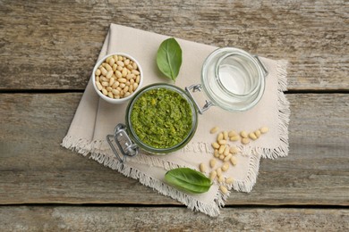 Photo of Delicious pesto sauce, pine nuts and basil leaves on wooden table, top view