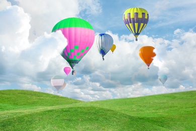 Image of Fantastic dreams. Hot air balloons in sky with fluffy clouds over green meadow