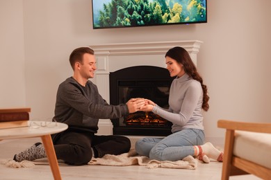 Photo of Happy lovely couple with hot drinks spending time together near fireplace at home